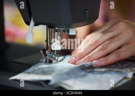 Caucasian young adult woman using sewing machine, hands guiding fabric under needle, focusing on precise stitching, close up of fingers and textile during garment creation Stock Photo