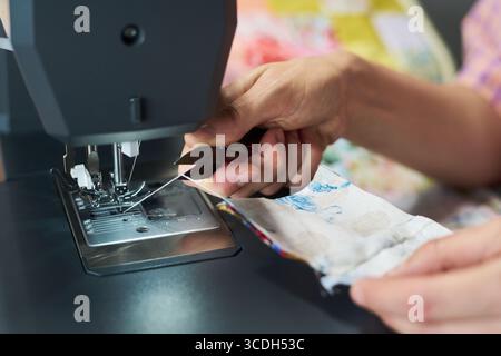 Caucasian woman using sewing machine, holding fabric and guiding needle with hands, focusing on precise stitching process, close up of hands and textile work Stock Photo