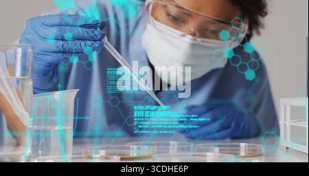 Woman scientist in PPE transferring sample using pipette over petri dish in lab with holograms Stock Photo