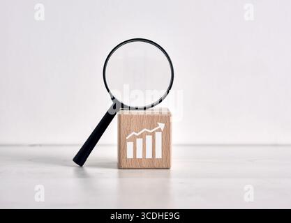 Magnifying glass leaning on wooden block with positive growth chart, representing business growth, financial analysis and market research Stock Photo
