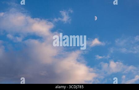 A large moon is visible in the sky above a cloudy blue sky. The moon is the only object in the sky, and it is the main focus of the image. The sky is Stock Photo