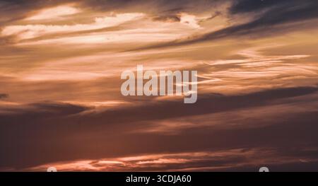 Fiery sky at sunset with soft clouds in an orange and red gradient, peaceful and vibrant atmosphere. Stock Photo