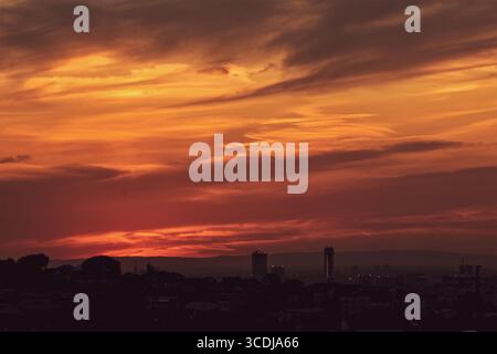 Intense red and orange sunset over modern city skyline, silhouettes glowing against vibrant sky. Stock Photo