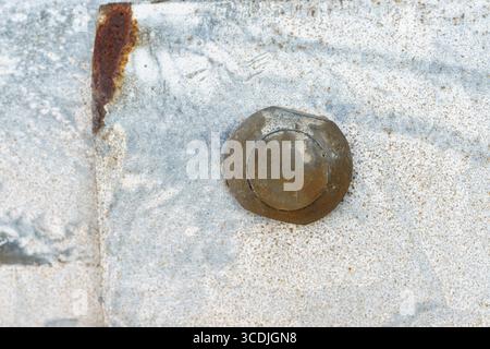 A rusty metal bolt is fixed into a weathered, textured surface with corrosion stains and light discoloration around it. Stock Photo