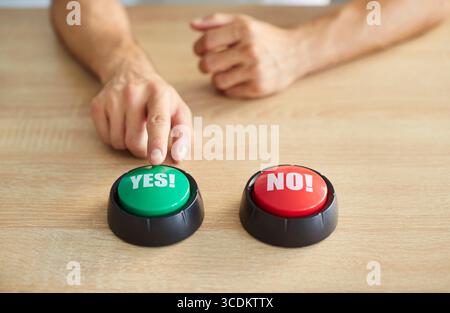 Person hands in moment of decision, finger pressing down on green yes button and contrasting red no Stock Photo