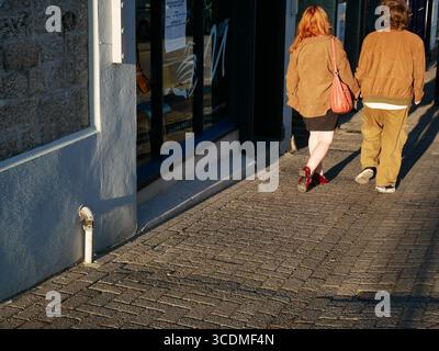 Young couple holding hands walking down the street in warm evening light. Stock Photo