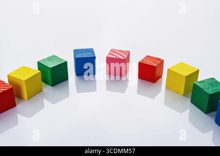 A creative arrangement of colorful wooden cubes in a curved line on a bright white surface. Stock Photo