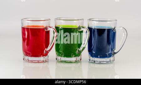 Three Glass Mugs Filled with Red, Green, and Blue Colorful Beverages on White Background Stock Photo