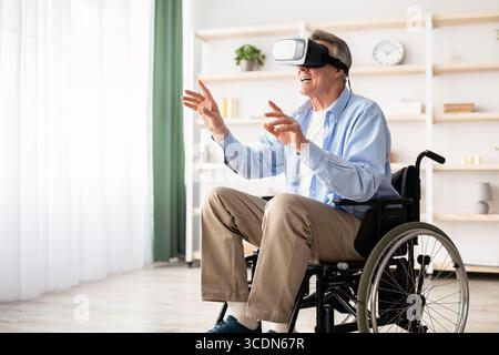 Happy handicapped senior man in wheelchair using VR headset to explore augmented reality at home Stock Photo