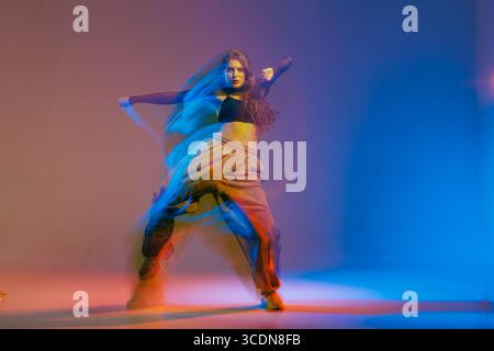 Confident jazz funk dancer in modern urban style performing expressive choreography with dynamic colorful lighting. Stock Photo