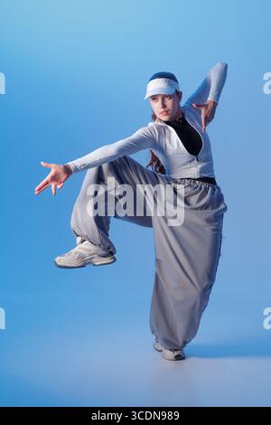 Young performer in jazz funk style striking a dynamic pose in baggy streetwear on a blue studio background ideal for dance and youth culture content Stock Photo