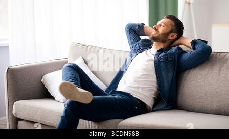 Happy bearded man relaxing on couch at home Stock Photo