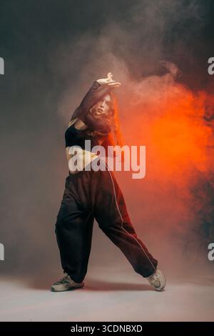 Confident jazz funk dancer in urban style pants, striking a dynamic pose with expressive movement and creative smoke effects. Stock Photo