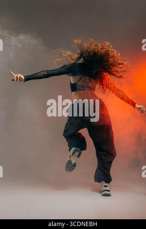 Confident jazz funk dancer in trendy outfit captured from the back, expressing movement with dramatic smoke effects. Stock Photo