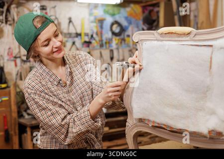 Woman repairing upholstered chair in workshop creative furniture restoration process carpentry and DIY project Stock Photo