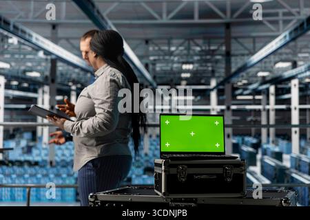 Team of data center admins using green screen notebook, testing, troubleshooting and repairing hardware. Server room coworkers walking in facility, doing brainstorming, using mockup laptop Stock Photo