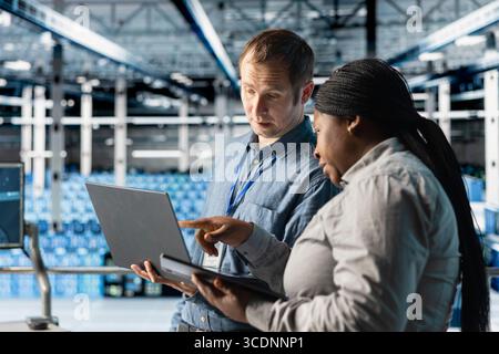 Team of data center admins using laptop to manage software updates for system stability. Teamworking server room IT specialists optimizing performance with device, configuring infrastructure Stock Photo