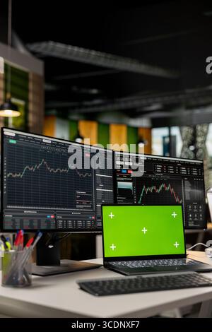 Close up of mockup laptop on desk and computer displaying candlestick graphs with stock market shares. Isolated screen notebook device and PC showing financial data analysis of stock exchange assets Stock Photo