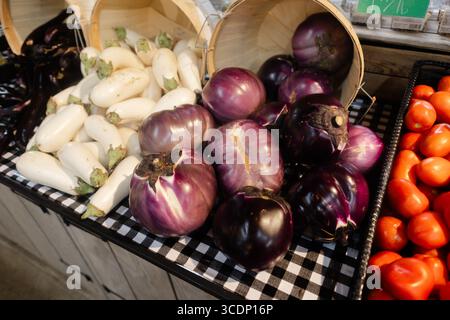 Colorful selection of eggplants and ripe tomatoes available for purchase at a vibrant farmer's market. Stock Photo