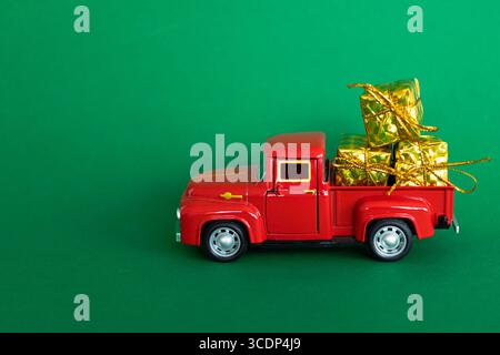 A red toy truck carrying gift boxes wrapped in gold paper, for Christmas, on a green background Stock Photo