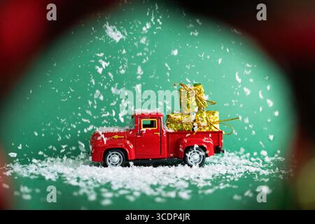 A red toy pickup truck carrying golden gifts under falling snow on a green background. Stock Photo
