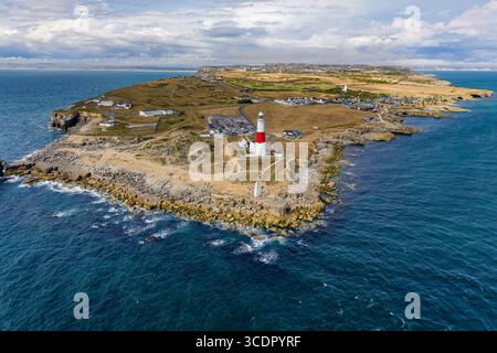 Aerial view of a lighthouse on a rocky outcrop surrounded by deep blue ...