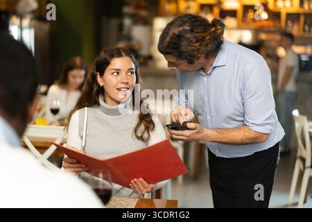Woman ordering from waiter sitting at table with man Stock Photo