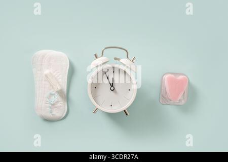 Female different tampons, daily pads, clock on blue background. Limited time use concept. Hygiene accessories for women. View from above. Stock Photo