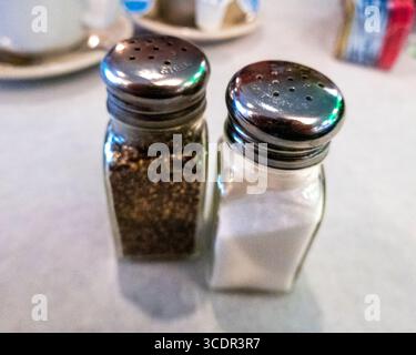 Close-up of glass salt and pepper shakers resting on a diner’s table, set atop a crisp white paper placemat, capturing a classic, timeless touch of ca Stock Photo