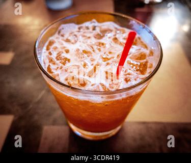 A classic chilled Mai tai cocktail served over crushed ice in a short glass, featuring a frothy orange hue and garnished with a red straw, set on a so Stock Photo