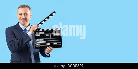 Mature actor holding movie clapper on blue background with space for text Stock Photo