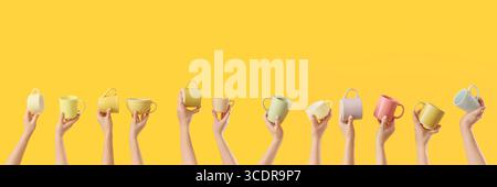 Many hands holding ceramic cups on yellow background Stock Photo