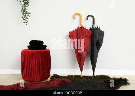 Hat on stylish pouf and umbrellas near light wall Stock Photo