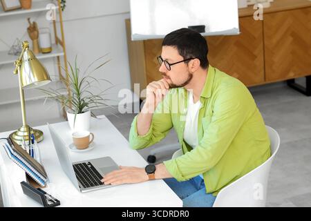 Focused young male teacher with laptop and cup of coffee giving online lesson at home Stock Photo
