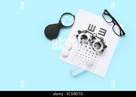 Optical trial frame with eye test chart, eyeglasses and magnifier on blue background Stock Photo