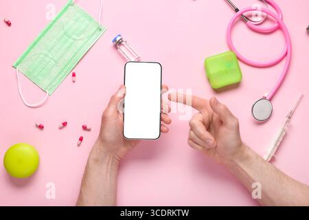 Male hands pointing at blank mobile phone and medical supplies on pink background Stock Photo