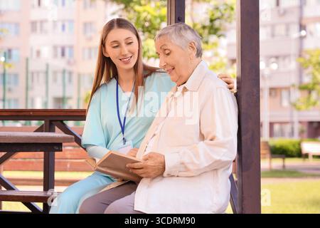 Senior woman with nurse reading book in gazebo outdoors Stock Photo