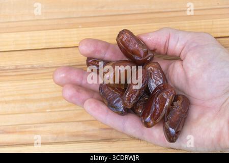Fresh Brown Dates in a Hand on Wooden Surface. Stock Photo