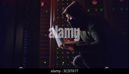 Mask, man or hacking with laptop for cybersecurity, programming or breach in night. Software attack, late or hacker with tech in dark room for big Stock Photo