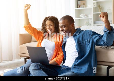 Joyful young African American couple with laptop celebrating success at home Stock Photo