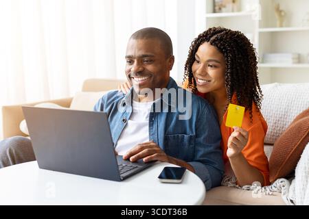 Happy young African American couple using laptop and credit card at home Stock Photo