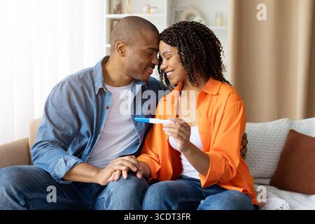 Happy African American couple sitting close together, holding pregnancy test and smiling Stock Photo