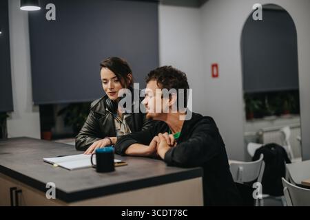 Two colleagues collaborating at a desk during a work session in a modern office space. Stock Photo