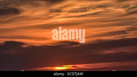 Abstract sunset sky with fiery tones fading into grey and misty cloud formations. Stock Photo