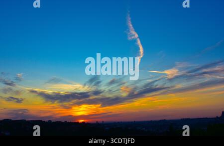 Abstract sky with soft orange-grey clouds and city skyline in silhouette at dusk. Stock Photo