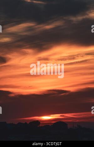 Abstract sky with soft orange-grey clouds and city skyline in silhouette at dusk. Stock Photo