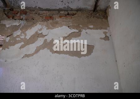 Close-up of peeling plaster revealing brickwork underneath in an old deteriorating building. Concept of renovation, decay, and construction defects. Stock Photo