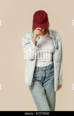 Serie of studio photos of woman in modern casual outfit, blue jeans, white tank top, denim overshirt red red baseball cap Stock Photo