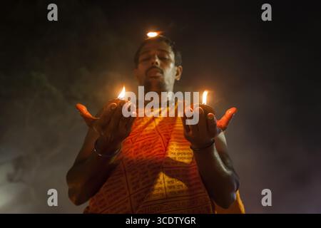 Narayanganj, Bangladesh - 15 November 2022: View of a man in traditional attire holding flames in his hands, a single flame dancing on his head, against a smoky backdrop. Stock Photo