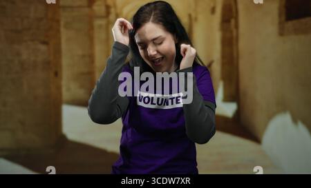 Woman dancing joyfully on university campus in volunteer shirt shows enthusiasm and positive energy. Stock Photo